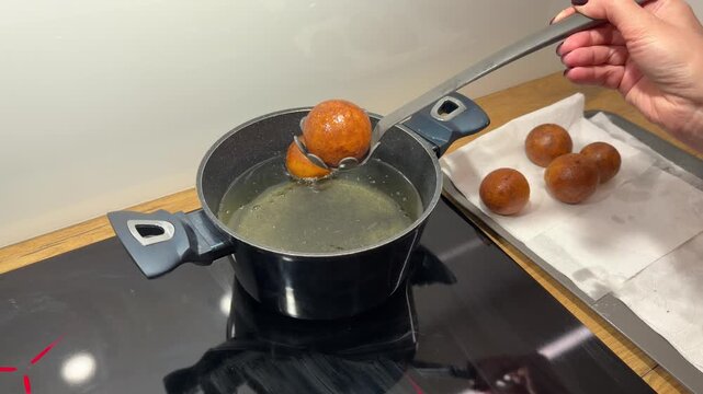 Removing Golden Dough Balls from Oil with Slotted Spoon. Close-up of hot golden dough balls being scooped out of frying pot. Spoon transfers finished treats to tray for cooling.