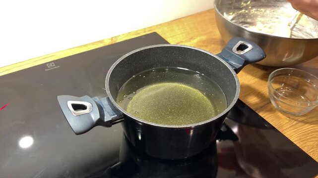 Dropping Raw Dough into Pot of Clear Hot Cooking Oil. Hand carefully places small piece of dough into pot of preheated oil on induction stove. Bubbles form instantly as frying process begins.