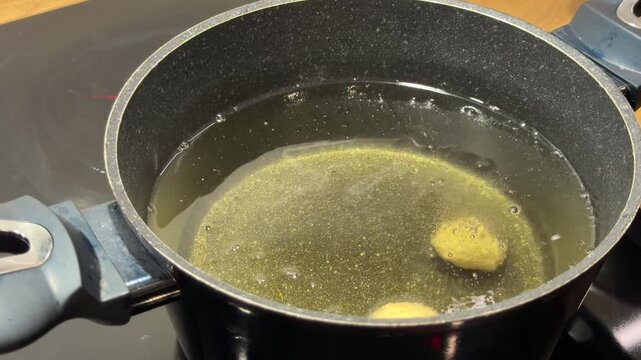 Small Dough Balls Beginning to Fry in Pot of Hot Oil. Raw dough pieces are dropped into hot oil and start to bubble and rise. Shot focuses on initial stage of deep frying in home kitchen.