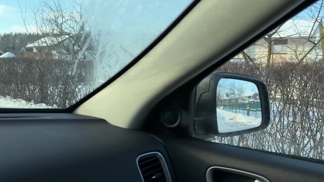 Driving Along Snowy Road with Residential Fences. POV from vehicle passing through quiet winter neighborhood with long hedges and fences. Sun reflects off deep snow covering yards and roadside.