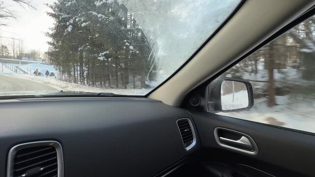 Driving Up Snowy Hill Past Modern Rural Houses. POV from car ascending winter road lined with contemporary homes and frosted deciduous trees. Landscape covered in thick untouched white snow.