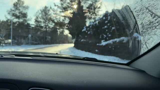 Driving into Bright Sun with Dirty Windshield. POV driving shot facing directly into bright winter sun highlighting smears on glass. Car travels along snowy road past fences in rural setting.