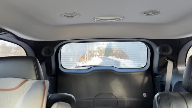 Interior View of Snowy Road Through Rear Car Window. Shot from inside back of moving vehicle looking out rear window at receding snowy road. Interior features black leather seats for cozy atmosphere.