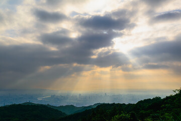 Fototapeta premium Stunning sunrise over Taipei City with god rays piercing clouds from Dadao Mountain in Shulin New Taipei City Taiwan featuring orange mist and green hills.