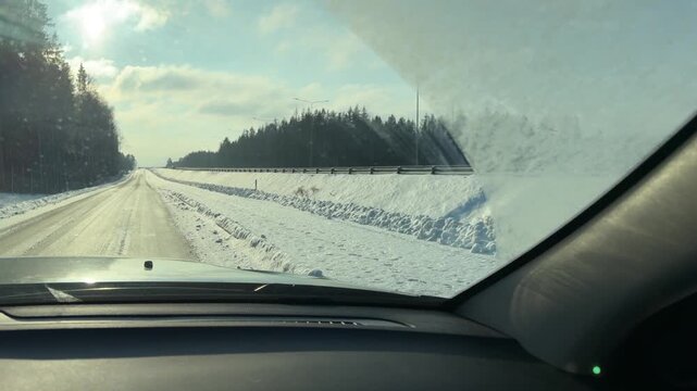 Winter Highway Driving with Sun and Snow Banks. Driving along highway with high snow banks on shoulder. Sun shines brightly from left casting shadows across road as car travels through forest area.