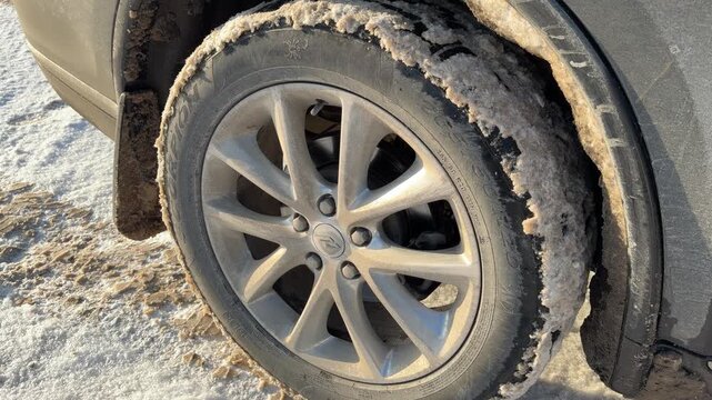 Frozen Slush on Car Tire and Rim. Detailed shot of car wheel showing ice and dirty snow accumulated on tire sidewall and alloy rim. Texture of frozen road grime highlights winter driving conditions.