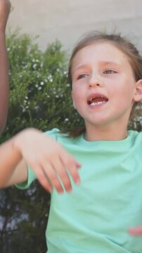 Vertical video: Singing left girl cueing right mirroring gestures for song by hedge in mint shirts