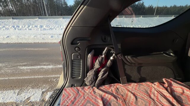 Closing Automatic Car Trunk Packed with Items. View of open SUV trunk containing umbrella and blanket. Hand reaches in to press automatic close button and tailgate lowers against snowy background.
