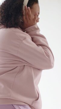 Vertical video: Adjusting white headset woman in hoodie turning, miming, swaying to music by window