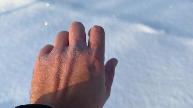 Hand Against Snowy Background in Winter. POV close-up of man's hand held up against blurred white snow background. Skin shows signs of cold exposure with natural texture and detail.
