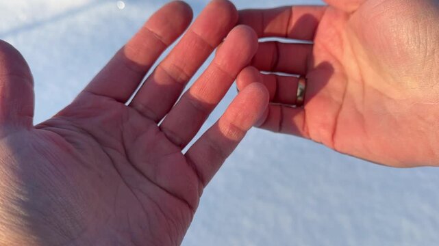 Man's Hand with Wedding Ring in Cold Weather. Close-up view of back of man's hand wearing gold wedding ring. Hand is held against bright white snow background showing dry skin from winter cold.
