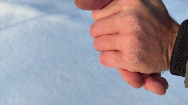 Warming Frozen Hands by Rubbing in Snow. Extreme close-up of man's hands briskly rubbing against each other to warm up. Skin is dry and red from harsh winter weather set against blurry snowy backdrop.