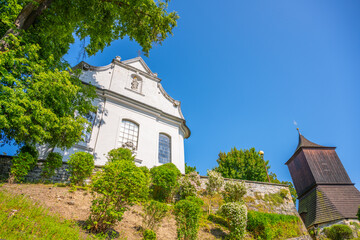 Visitors walk up the hill toward Church of St. James the Greater in Zelezny Brod. The church stands tall under a clear blue sky. Green trees surround the area.