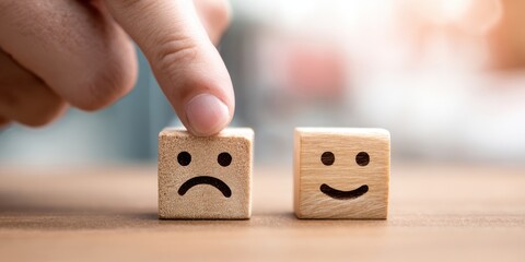 The wooden blocks with sad and happy faces and a finger selecting emotion