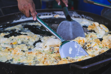 Thai crispy oyster omelet cooking on a large flat griddle.