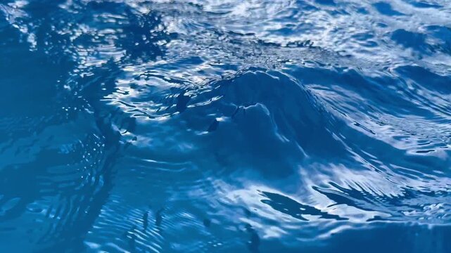 Detailed close-up view of a blue swimming pool water surface with ripples and sun reflections. Concept of clean water, abstract background, and resort relaxation. 4k 60fps, High frame rate 
