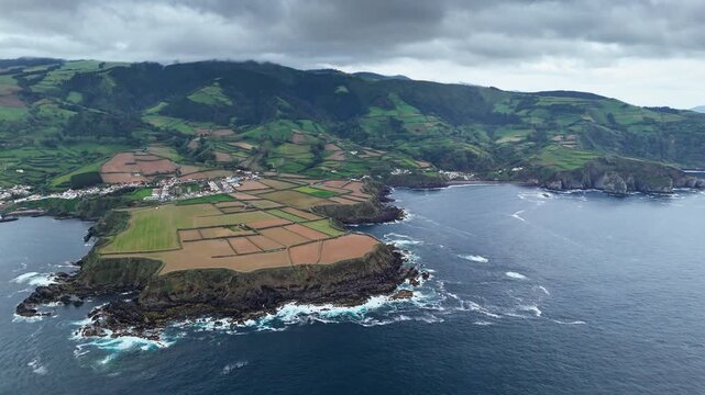 Terraced fields atop volcanic promontory with dark basalt formations and rough Atlantic waters, drone footage