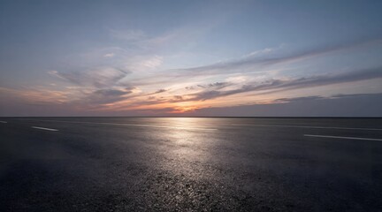 Empty highway stretches out under a sky painted with hues of orange at sunset