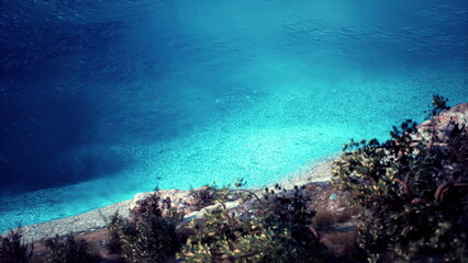 Fototapeta premium Gentle waves lap at a tranquil shoreline where vibrant blue waters meet a pebbled beach. Lush trees frame the scene, creating a peaceful retreat in natures embrace.