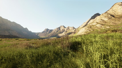 Majestic mountains rise sharply against the horizon, surrounded by vibrant green grass. The sky glows softly in the morning light, creating a serene atmosphere of natural beauty.