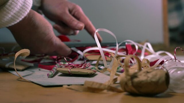 Christmas gift wrapped in string with hands using mobile phone in background