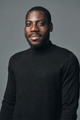 Obraz premium African American man with dark skin wearing black turtleneck sweater posing with confident smile in creative visual designer style studio portrait on gray background.