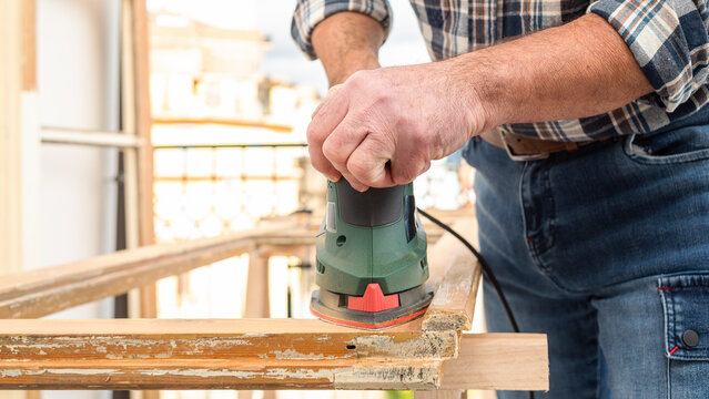 Craftsman. Adult carpenter using an electric sander to smooth an old wooden window. Construction industry, carpentry, housework do it yourself. Restoration.