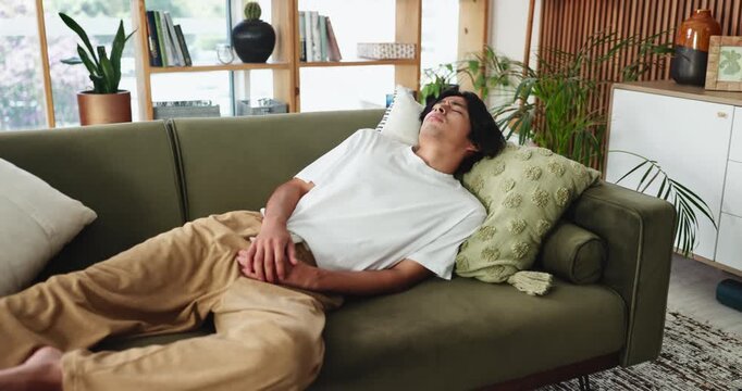 Man, stomach ache and sofa with diarrhea, pain or gastrointestinal reflux in home. Asian, male person or lying with virus, sore belly or cramp for food poisoning, indigestion or sickness in house