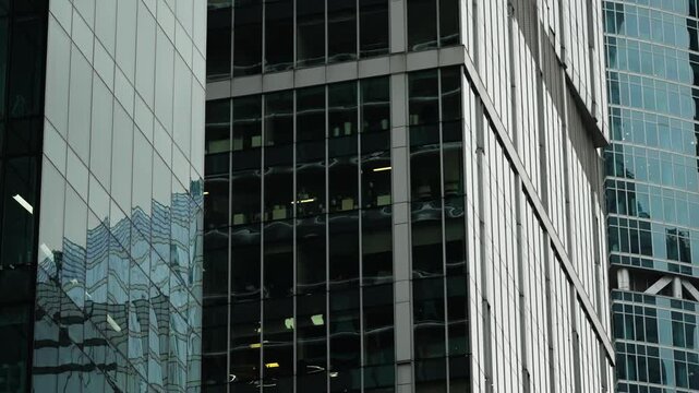 Close-up of modern glass and steel skyscraper facades with reflective windows, geometric lines, and urban textures revealing office interiors in neighboring high-rise towers