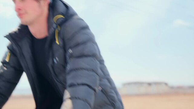 white male cyclist riding rural road in puffy jacket and headband -  steady pedaling -  mountain bike wheels kicking dust -  barren fields and pale sky conveying focused endurance and crisp cold