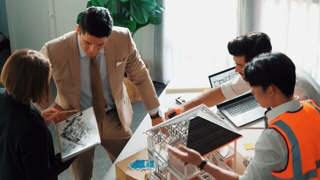 Top view of professional architect engineer team inspect house model while manager holding blueprint and asking about building construction. Group of diverse engineer working together. Alimentation.