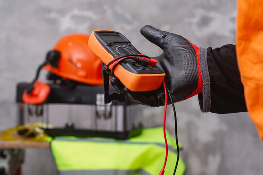 Electrician wearing protective gloves holding digital multimeter for electrical testing and diagnostics. Concept of professional electrical service, voltage measurement and equipment inspection.