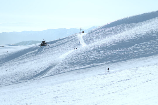 Minimal winter landscape of skiers climbing a snowy slope at La Parva Ski Resort in the Chilean Andes. The scene features bright sunlight, expansive snow fields and distant mountain layers.