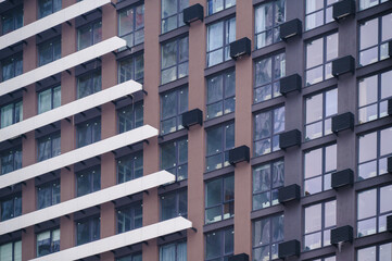 Modern apartment building showcasing a geometric facade with brown and dark grey sections, numerous windows, and structured balconies creating a patterned urban design