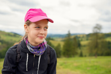 Pensive Teenage Girl in Pink Cap and Plaid Scarf Gazes over Green Rolling Hills, Backpack On, Cloudy Countryside Portrait