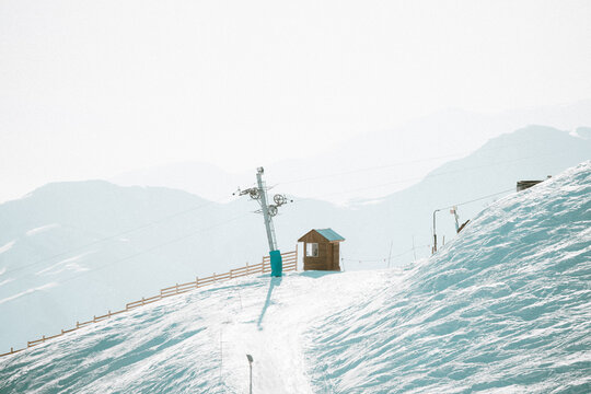 Minimal winter landscape showing a ski lift tower and a small wooden cabin on a snowy slope at La Parva Ski Resort in the Chilean Andes. The scene features soft light and distant mountain layers.
