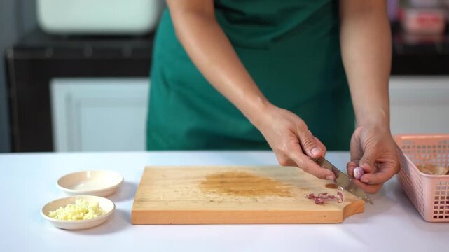 Close up of hands peeling and slicing shallots on a wooden cutting board