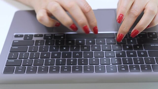 Woman is typing on a laptop keyboard with red fingernails. The keyboard has a number pad and a space bar