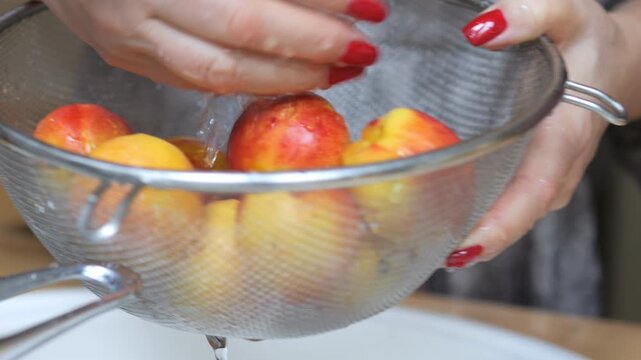 Woman is washing apples in a colander. The apples are in the colander and the water is running over them