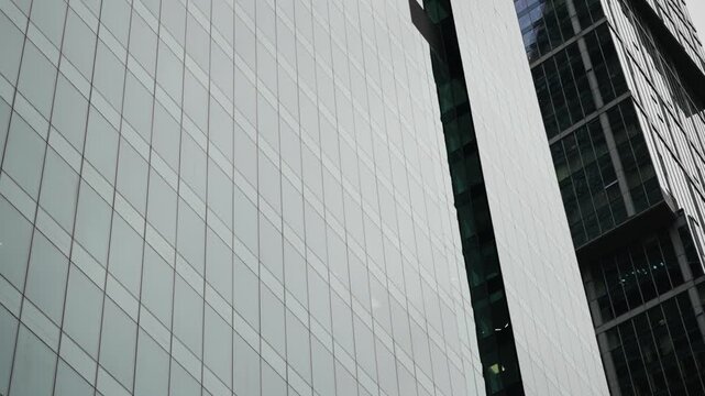 Close-up view of sleek glass-clad skyscraper facades with repeating window grid patterns, vertical lines, and reflective surfaces in a modern urban business district