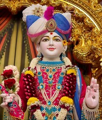 Obraz premium Beautiful close-up view of indian lord or god swaminarayan face glow, smile and blessing idol in the temple. isolated blurry multicolor designed costume, curtains and gold interior view in background.