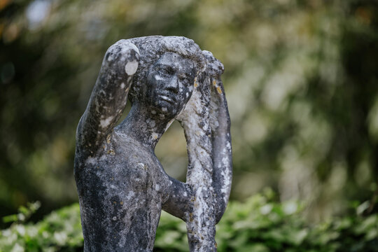 Weathered stone statue with braided hair in garden