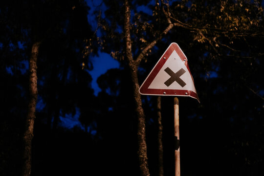 Road sign with intersecting roads symbol at night