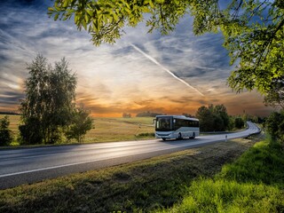 A white bus driving on the asphalt road in rural landscape at sunset © am