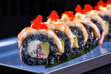 Close-up of premium sushi rolls with black rice, shrimp, avocado, and cream cheese, topped with Japanese mayonnaise and bright red tobiko caviar