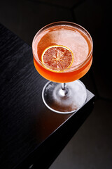Elegant orange cocktail in a chilled coupe glass on a dark minimalist background.