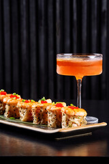 Gourmet sushi rolls topped with caviar and shrimp served with an orange cocktail on a dark background.