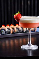 Gourmet sushi rolls topped with caviar and shrimp served with an orange cocktail on a dark background.