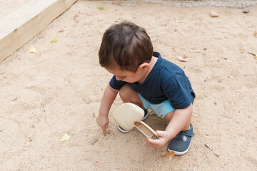 Toddler boy playing with sand in outdoor sandbox