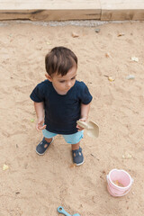 Toddler boy playing with sand in sandbox outdoors